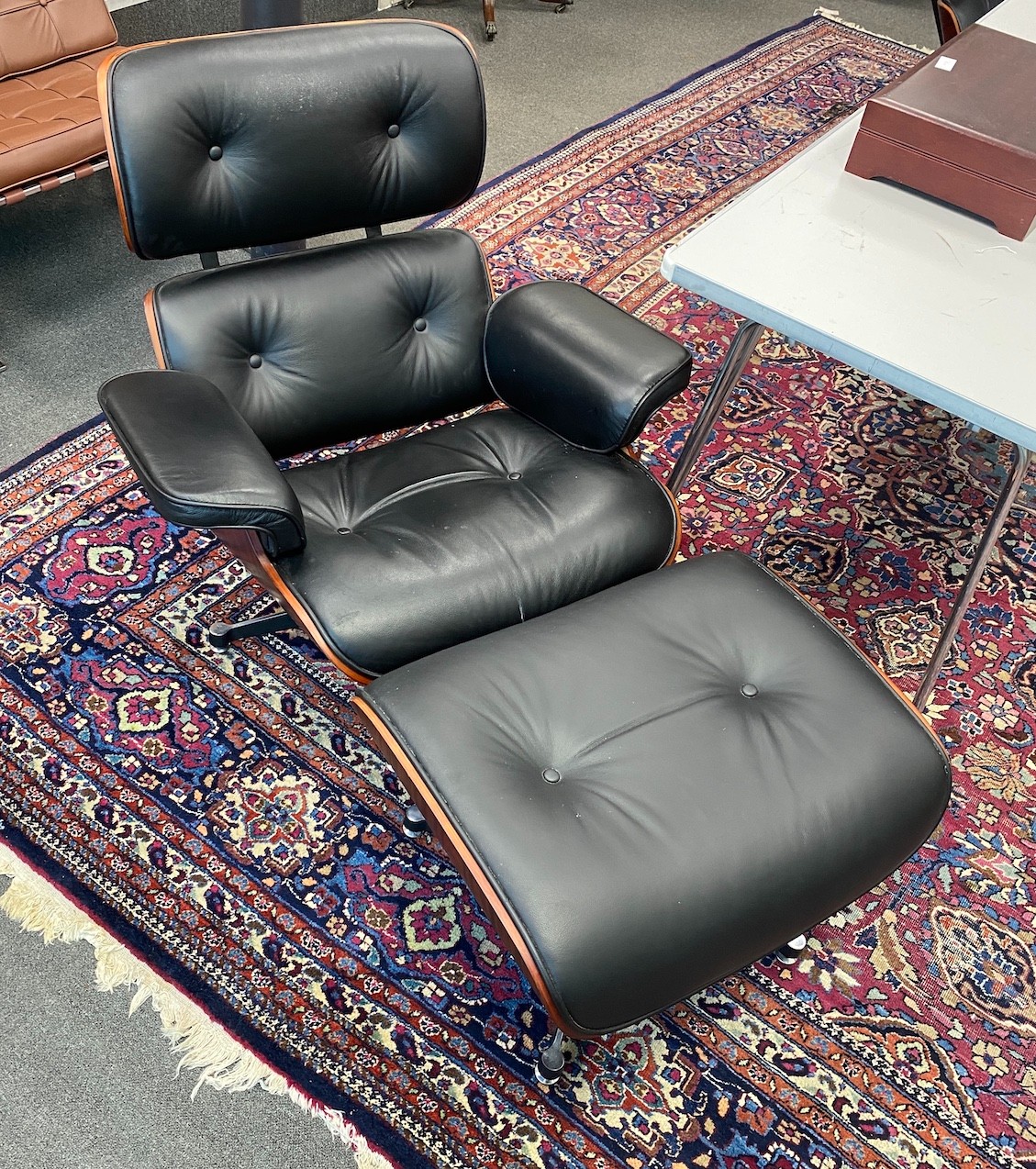 A pair of Eames style black leather, simulated rosewood swivel lounge chairs and footstools